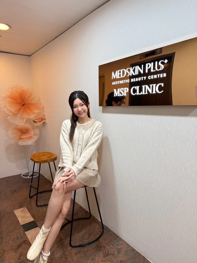 一位穿米白色針織上衣的女士坐在診所高腳椅上微笑，旁邊牆身掛有 MEDSKIN PLUS+ 美學中心及 MSP CLINIC 招牌。