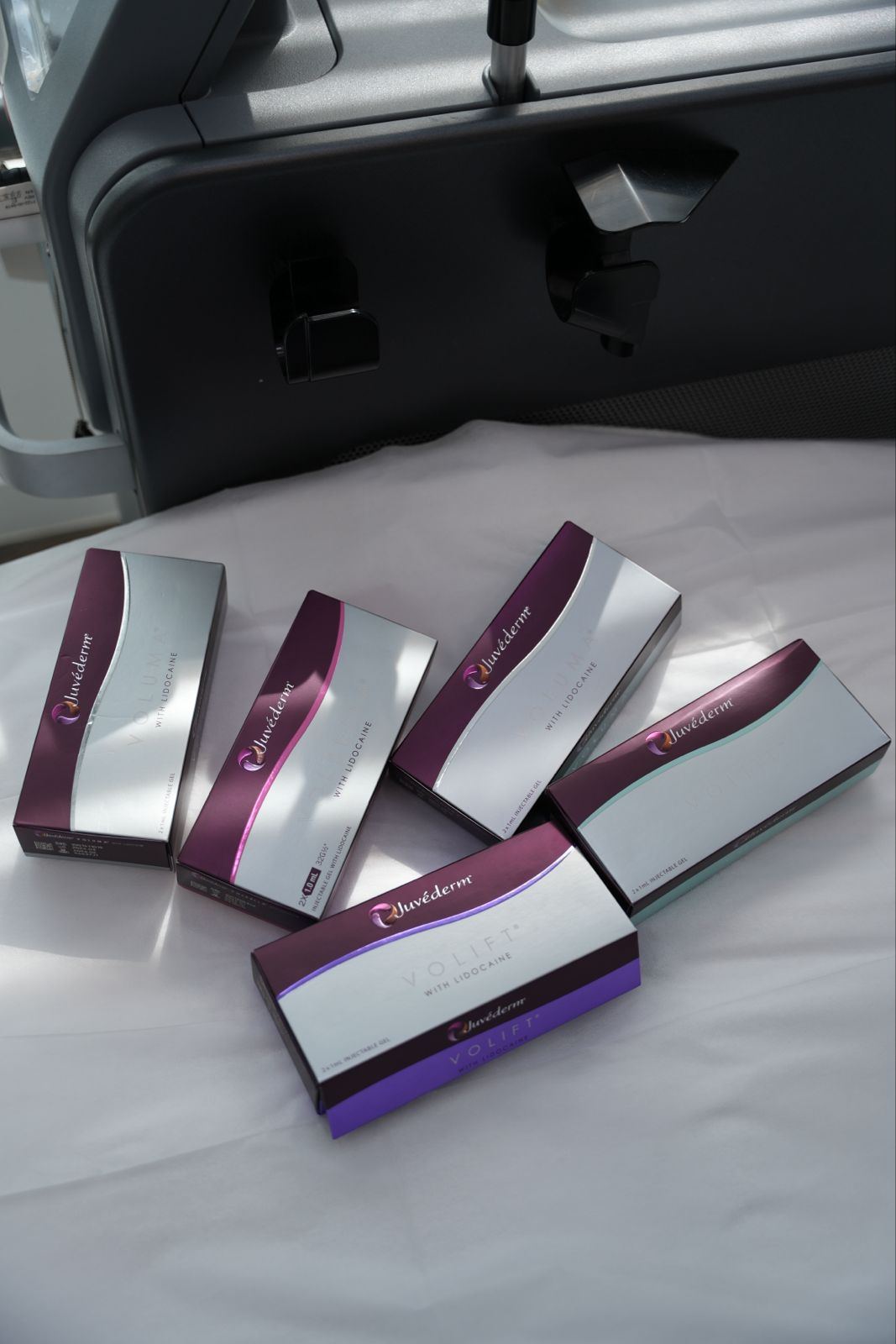 白色床單上斜放五盒 Juvederm 透明質酸填充劑，盒面為銀紫雙色設計並印有 VYCROSS 及 VOLIFT 字樣，背景可見深灰色診所儀器。