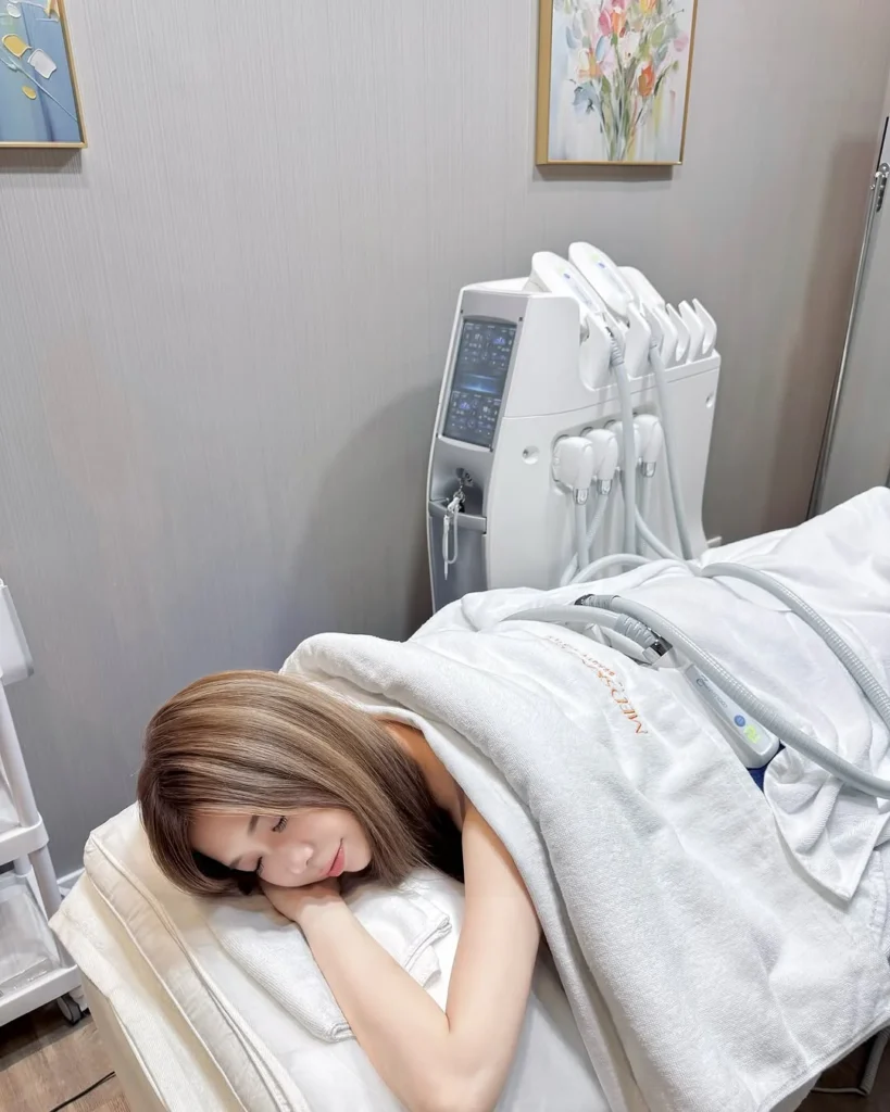 一名淺棕色短髮女性側躺於治療床上微笑，身上蓋著印有 MEDSKIN PLUS+ 字樣的白色毛巾，房內有花藝掛畫與白色儀器。